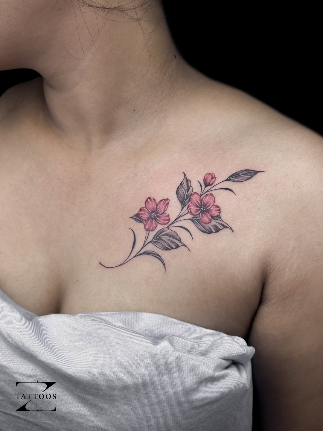 Delicate red cherry blossoms with grey leaves on a collarbone, fine-line colour work.